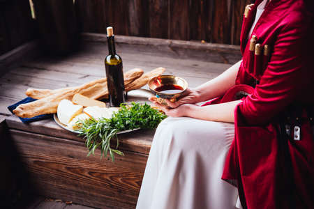 Young beautiful girl wearing traditional georgian dress holds a tray full of traditional georgian food: cheese, bread, greens and wine.の写真素材