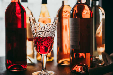 A glass and different bottles of wine served on a wooden table in a bar or a wine shop.の写真素材