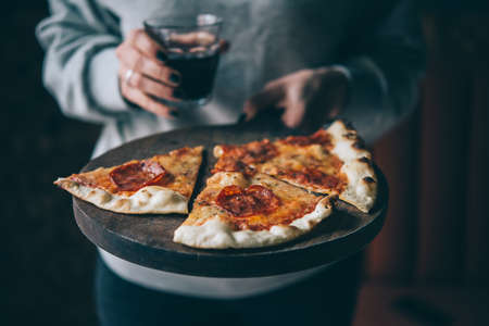 Hands holding a board with pizza pepperoni and a glass of wine. Toned pictureの写真素材