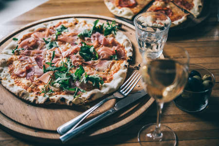 Delicious prosciutto ham pizza served with a glass of wine on a wooden table for dinner.の写真素材
