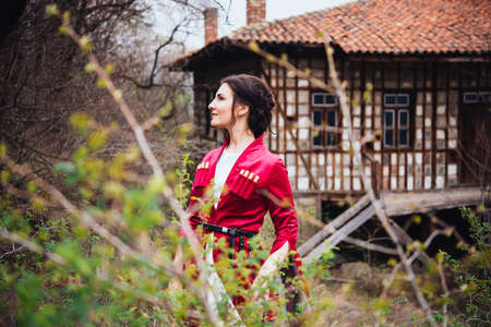 Young beautiful girl wearing traditional georgian dress stands in front of georgian house.の写真素材