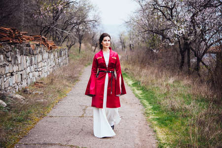 Young beautiful girl wearing traditional georgian dress walks along the village.の写真素材
