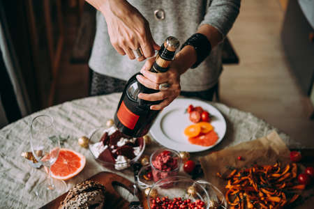 Woman opens bottle of champagne. Dinner table, celebrating Christmas or New Year eveの写真素材