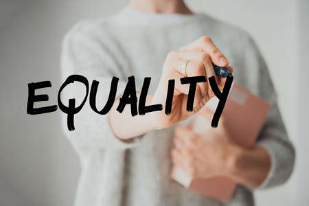 Writing hand. Woman holds pen or marker and writing Equality wordの写真素材