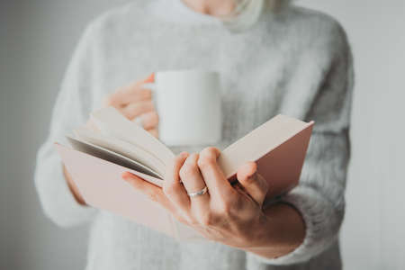 Girl holding a book and a cup of coffee or tea in her hands. Education or reading concept