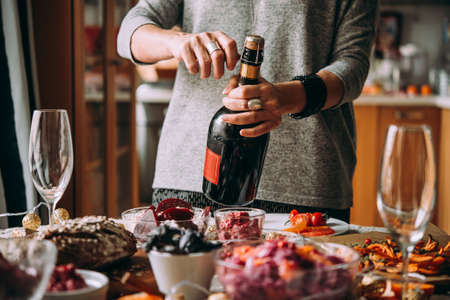 Woman opens bottle of champagne. Dinner table, celebrating Christmas or New Year eveの写真素材