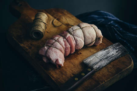 A small home-made porchetta on a wooden board ready for baking.の写真素材