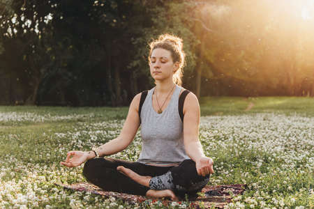 A young beautiful woman is meditating or practising yoga outdoors. Outdoor recreation concept.の写真素材