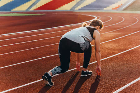 A young beautiful woman in a starting position at a stadium running track.の写真素材