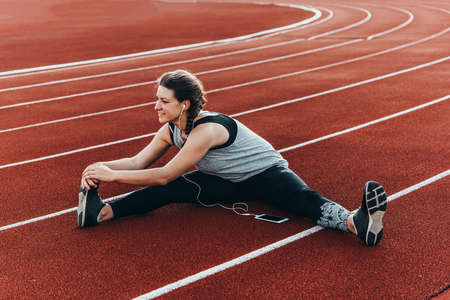 A young beautiful woman enjoys stretching at a stadium running track.の写真素材