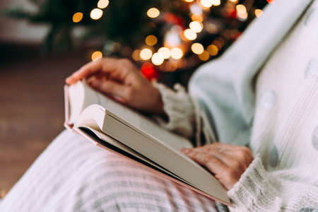 A young woman is reading a book sitting by the Christmas tree.の写真素材