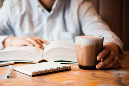 A person having a cup of coffee and reading a book in a cafeの写真素材