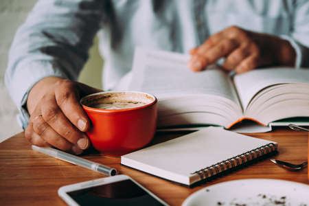 A person having a cup of coffee and reading a book in a cafeの写真素材