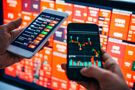Traders or financial analysts checking the recent stock exchange trends using their smartphones.の写真素材