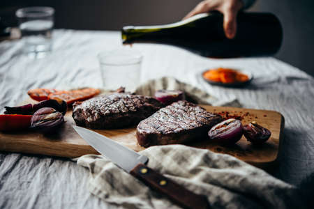 Pouring red wine for dinner with steaks and tomato salad. Healthy home eating concept.の写真素材