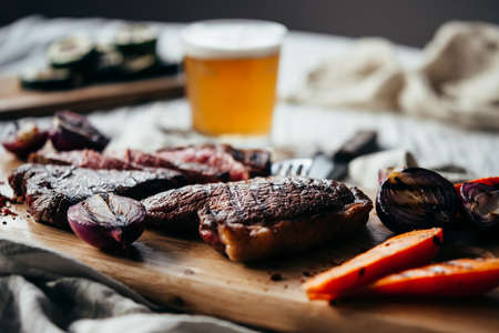 Pouring beer for dinner with steaks and grilled vegetables. Healthy home eating concept.の写真素材