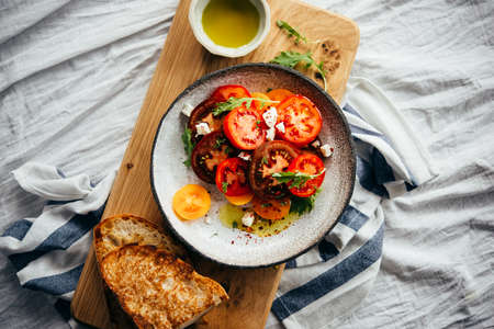 Home-made lunch of tomato salad and artisanal bread with olive oil served on a wooden board. Healthy...