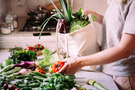 Unpacking a bag of fresh vegetables and greens after grocery shopping. Healthy eating concept.の写真素材