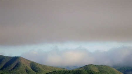 A somber and dark cloud jet steam over vividly bright hill range.の写真素材