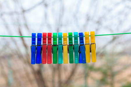 Row of colorful clothespins hanging on a green rope in a gerden with blurred background