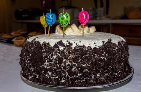 birthday cake with four candles decorated with banana slices and chocolate chips seen from sideの写真素材