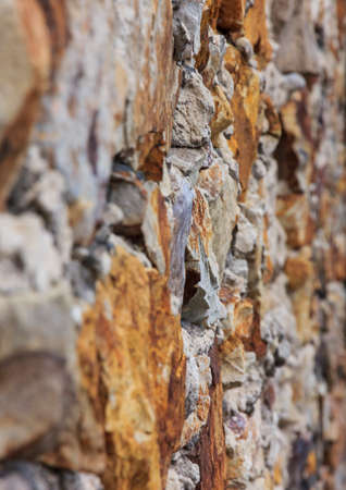 vertical photo of a fragment of old stone wall composed of stones of various sizes and shades seen from angle, with only central stones in focusの写真素材