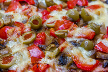 Close up photo of the surface of homemade pizza with slices of sausage; olives; paprika and melted cheeseの写真素材