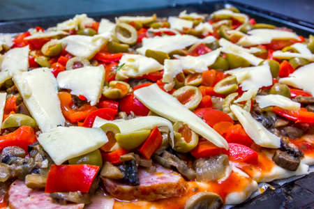 surface of pizza prepared for baking with raw slices of olives, sausage,  paprika and cheeseの写真素材