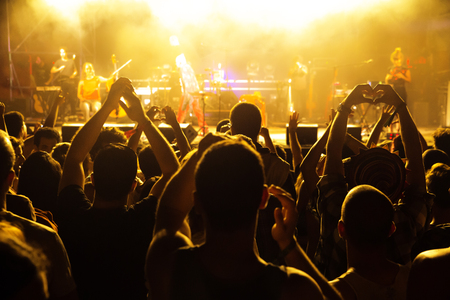 Crowd of people in front of stage at live concert. Fans cheering and raising their hands.の写真素材