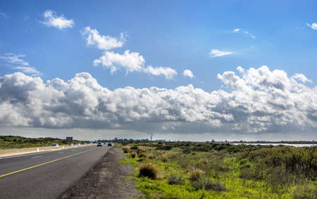 Highway passing through green rural landscape and blue sky with majestic clouds in the background.の写真素材