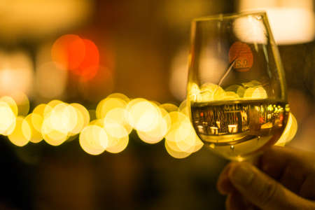 Hand holding a glass of white wine with lights in the backgroundの写真素材