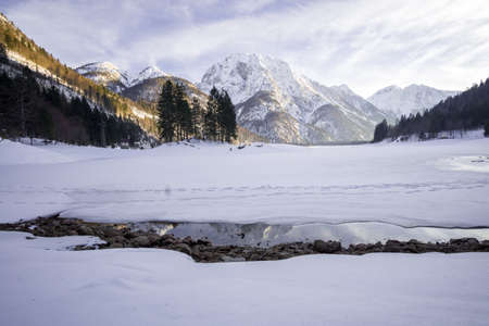 Frozen lake covered in snow with snowy mountain in the backの写真素材