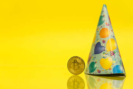 Bitcoin cryptocurrency celebrating birthday - 10 years, coin with birthday hat behind it, with yellow copy spaceの写真素材