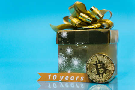 Bitcoin celebrating birthday, coin with birthday golden present behind it and 10 years sign, with blue copy spaceの写真素材