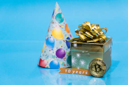 Bitcoin 10 year anniversary, coin with birthday golden present and birthday hat behind it and 10 years sign, copy spaceの写真素材