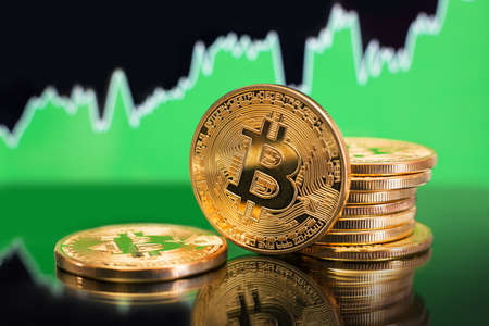 Stack of Bitcoin gold coins in front of a green bullish trend chart. Price rise concept.の写真素材