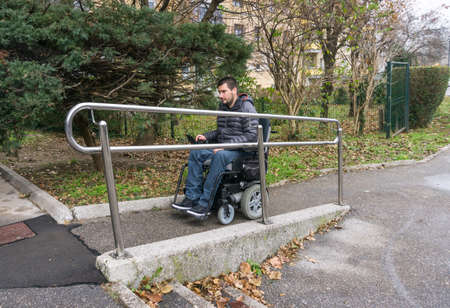 Man in a wheelchair using a ramp next to stairsの写真素材