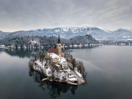 Aerial shot of lake Bled on a calm winter morning with snowの写真素材