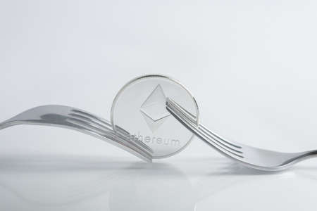 Ethereum cryptocurreny coin placed between forks with reflection, hard fork on white backgroundの写真素材