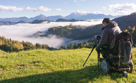 man on wheelchair taking photos of beautiful landscape in a foggy morning, St. Thomas Sloveniaの写真素材