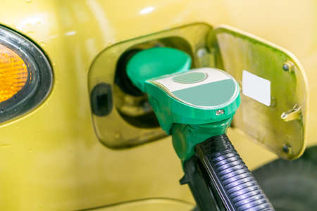 Yellow, gold car at a gas station being filled with fuel