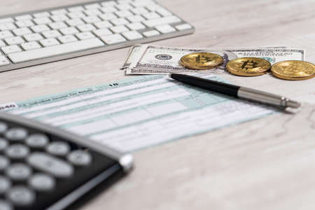 The pen, bitcoins, dollar bills and calculator on the tax form 1040 U.S next to computer keyboard. Individual Income Tax Return. The time to pay taxesの写真素材