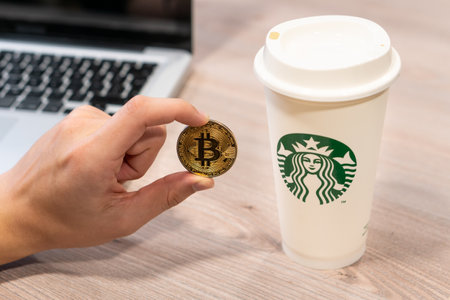 Cryptocurrency Bitcoin held by a humand hand next to Starbucks coffee cup. Slovenia 13.02.2019のeditorial素材
