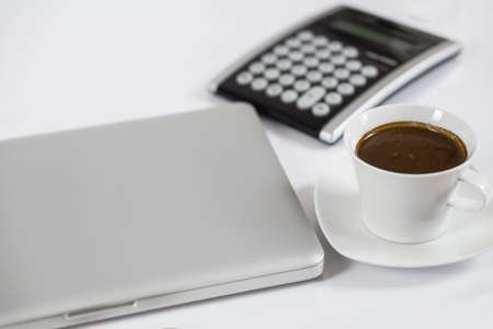 Business work place with cup of coffee calculator and closed computer laptop
