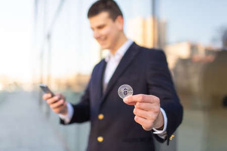 Ethereum cryptocurrency coin in a young businessman hand. Disruptive blockchain technology concept and transfer of wealth.の写真素材