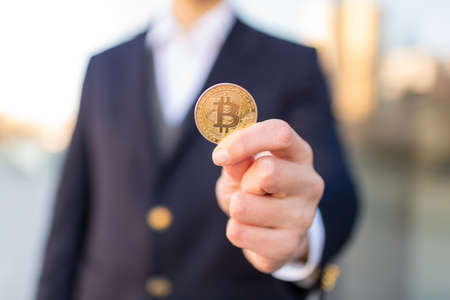 Bitcoin cryptocurrency coin in a young businessman hand. Disruptive blockchain technology concept and transfer of wealth.の写真素材