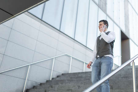 Young and Casual Businessman Using Smartphone while Walking Outside of Office Building