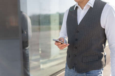 Young and Casual Businessman Using Smartphone while Walking Outside of Office Buildingの写真素材