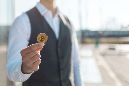 Bitcoin cryptocurrency coin in a young businessman hand. Disruptive blockchain technology concept and transfer of wealth.の写真素材