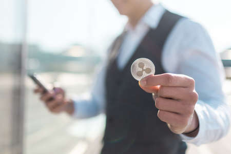 Ripple cryptocurrency coin in a young businessman hand. Disruptive blockchain technology concept and transfer of wealth.の写真素材